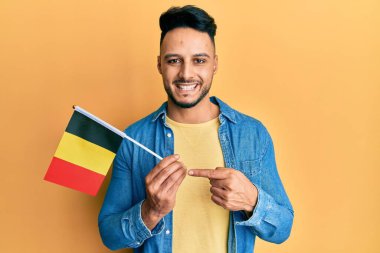 Young arab man holding belgium flag smiling happy pointing with hand and finger 