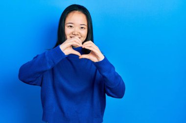 Sıradan kıyafetler giyen genç Çinli bir kız. Âşık bir şekilde gülümsüyor. Elleriyle kalp sembolü yapıyor. romantik kavram. 