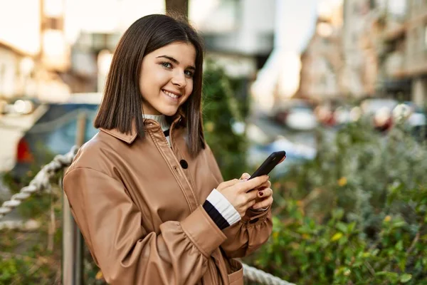 Genç, güzel esmer kadın dışarıda mutlu bir şekilde gülümsüyor akıllı telefon kullanıyor.