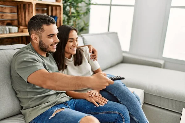 一对年轻的拉丁夫妇笑着高兴地在家里看电视 — 图库照片