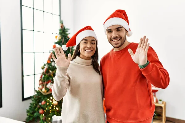 Young Hispanic Couple Standing Christmas Tree Waiving Saying Hello Happy — Stockfoto