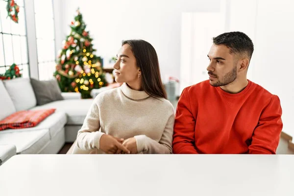 Young Hispanic Couple Sitting Table Christmas Tree Looking Side Relax — 스톡 사진