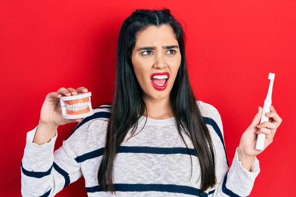 Young Hispanic Girl Holding Electric Toothbrush Denture Angry Mad Screaming — ストック写真