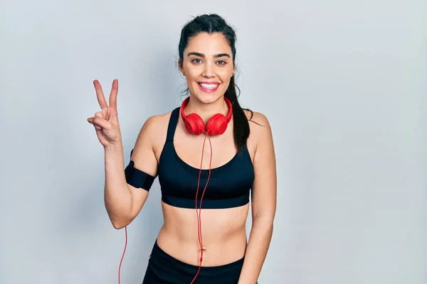 Young Hispanic Girl Wearing Gym Clothes Using Headphones Showing Pointing — 스톡 사진