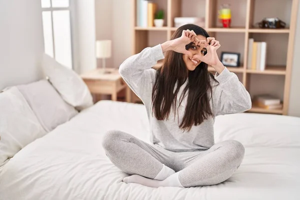 Young Hispanic Woman Doing Heart Gesture Sitting Bed Bedroom – stockfoto