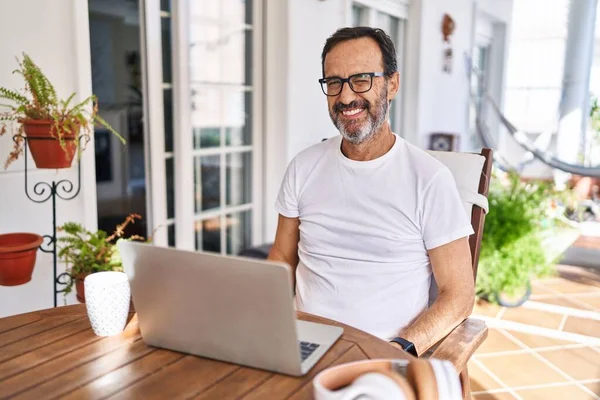 Orta yaşlı bir adam evde bilgisayar kullanıyor. Kameraya seksi bir ifadeyle bakıyor. Neşeli ve mutlu bir yüzü var.. 