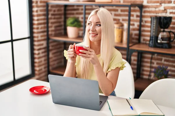 Νεαρή Ξανθιά Γυναίκα Που Χρησιμοποιεί Φορητό Υπολογιστή Πίνοντας Καφέ Κάθεται — Φωτογραφία Αρχείου