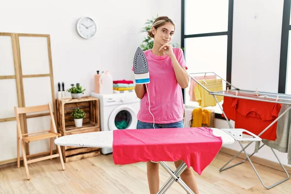 Young Blonde Woman Ironing Clothes Home Serious Face Thinking Question — Stockfoto