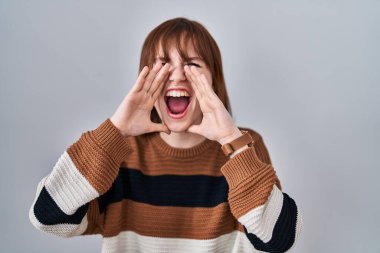 İzole edilmiş arka planda çizgili süveter giyen genç ve güzel bir kadın elleri ağzında kızgın bir şekilde bağırıyor. 