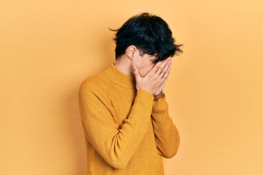 Yakışıklı hippi genç adam gündelik sarı süveter giyiyor ve ağlarken suratını ellerle kapatıyor. depresyon kavramı. 