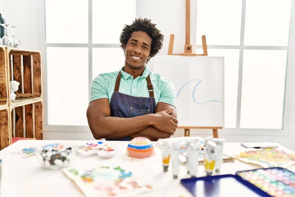 若いアフリカ系アメリカ人の男性は アートスタジオのテーブルの上にカメラを見て両腕を組んで笑顔で座っている 正の人 — ストック写真