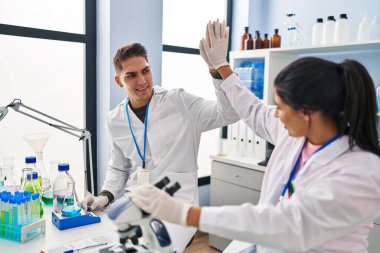 Erkek ve kadın bilim adamları laboratuarda elleri havada beşlik çakıyor.