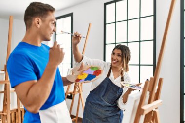 Resim okulunda boya fırçasıyla oynarken gülümseyen iki öğrenci..