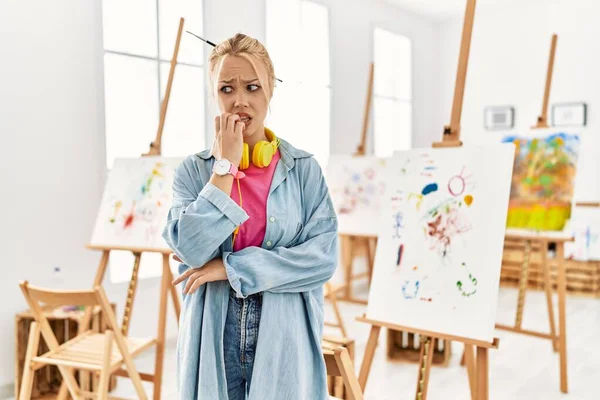 Young caucasian girl at art studio looking stressed and nervous with hands on mouth biting nails. anxiety problem.