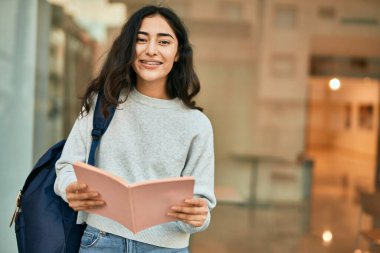 Genç ortadoğu öğrencisi kız şehirde mutlu bir şekilde kitap okuyor..
