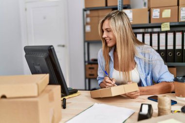 Genç sarışın kadın ecommerce iş işçisi ofiste paket üzerine yazıyor.