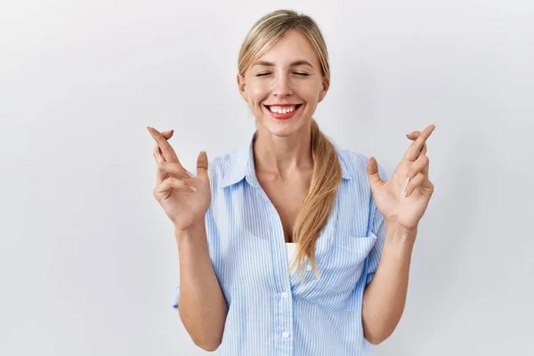 Mooie Blonde Vrouw Staat Witte Achtergrond Gebaren Vinger Gekruist Glimlachen — Stockfoto