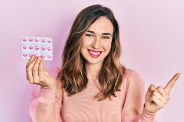 Genç İspanyol kız elinde haplarla gülümsüyor mutlu bir şekilde elini ve parmağını yana uzatıyordu. 