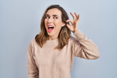 Young woman standing over isolated background smiling with hand over ear listening an hearing to rumor or gossip. deafness concept. 