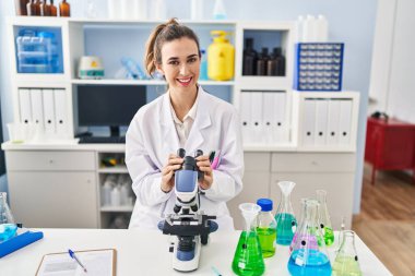 Young woman wearing scientist uniform using microscope at laboratory