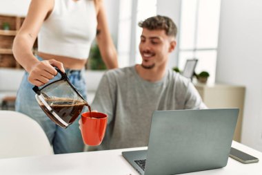 Adam evde dizüstü bilgisayarla çalışıyor ve kız arkadaşı kahve dolduruyor..