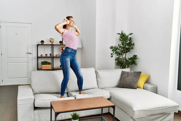 Young woman listening to music and dancing standing on sofa at home