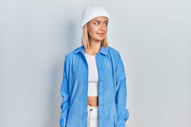 Yün şapka takan güzel sarışın kadın gülümsüyor, yan tarafa bakıyor ve düşünüyor.. 