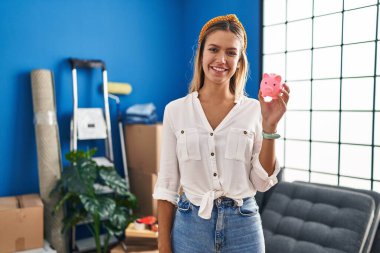 Genç sarışın kadın elinde kumbarayla yeni bir eve taşınıyor. Olumlu ve mutlu görünüyor. Kendine güvenen bir gülümsemeyle dişlerini gösteriyor. 