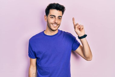 Gündelik tişört giyen genç İspanyol adam başarılı bir fikri işaret ediyor. Heyecanlı ve mutlu. Bir numara.. 