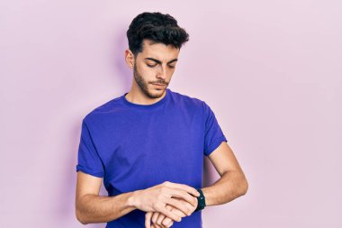 Gündelik tişört giyen genç İspanyol adam kol saatini kontrol ediyor, rahat ve kendinden emin. 
