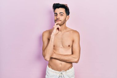 Mayo giyen genç İspanyol adam kameraya kendinden emin bir şekilde bakıyor kollarını kavuşturmuş ve çenesini kaldırmış şekilde gülümsüyor. Olumlu düşünmek. 