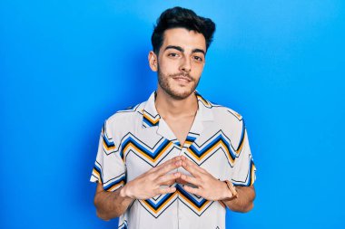 Latin asıllı genç adam rahat ve neşeli gülümseyerek ellerini birleştirip gülümsedi. Başarı ve iyimserlik 