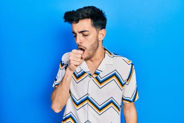 Günlük kıyafetler giyen genç İspanyol adam kendini iyi hissetmiyor ve soğuk algınlığı veya bronşitin belirtisi olarak öksürüyor. sağlık hizmeti kavramı. 