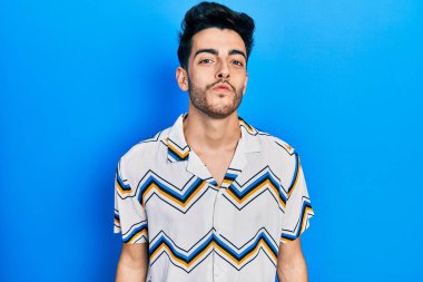 Latin asıllı genç bir adam, günlük giysiler içinde kameraya bakıyor ve güzel ve seksi bir şekilde havadan öpücük yolluyor. aşk ifadesi. 