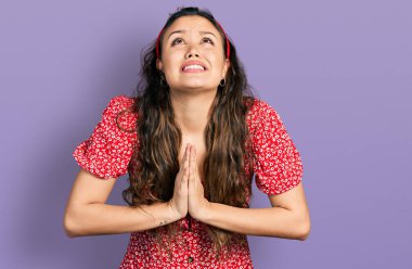 Gündelik giysiler giyen genç İspanyol kız elleri ile yalvarıyor ve dua ediyor. Yüzünde umut ifadesi var. Çok duygusal ve endişeli. Yalvarıyor. 