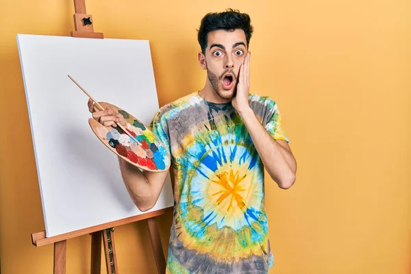 Genç, İspanyol asıllı bir adam palet üstüne palet çizerek ayakta duruyor. Korkuyor ve şoka uğruyor. Şaşırıyor ve şaşırıyor. 