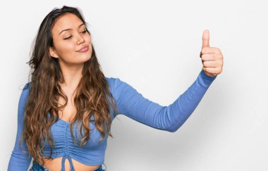 Gündelik kıyafetler giyen, gururlu görünen, gülümseyen genç İspanyol kız yan tarafa baş parmak hareketi yapıyor. 