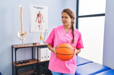 Fizyoterapi kliniğinde çalışan genç İspanyol kadın basketbol topu tutuyor ve kafası karışık. şüphe kavramı. 