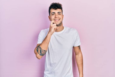 Günlük beyaz tişört giyen genç İspanyol adam kameraya kollarını kavuşturmuş ve çenesi üzerinde kendinden emin bir şekilde bakıyor. Olumlu düşünmek. 