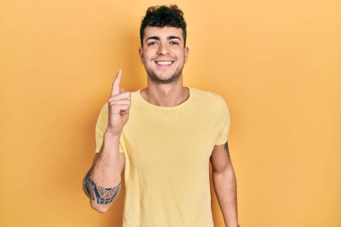 Gündelik tişört giyen genç İspanyol bir adam bir fikir ya da soruyla gülümsüyor ve mutlu bir yüzle işaret ediyor. 