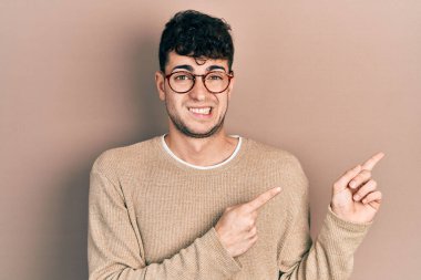 Gündelik kıyafet ve gözlük takan genç İspanyol bir adam iki eliyle endişeli ve gergin, endişeli ve şaşırmış ifadesini işaret ediyor. 