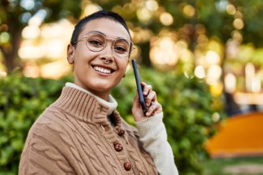 Kısa saçlı, gülümseyen, telefonda konuşan genç İspanyol kadın.