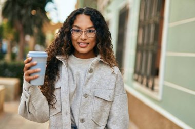 Genç Latin kadın gülümsüyor, şehirde kahve içiyor..