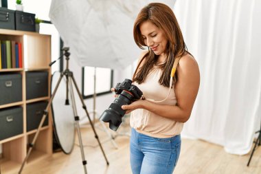 Genç İspanyol fotoğrafçı kadın fotoğraf stüdyosunda kamerayla mutlu bir şekilde gülümsüyor..