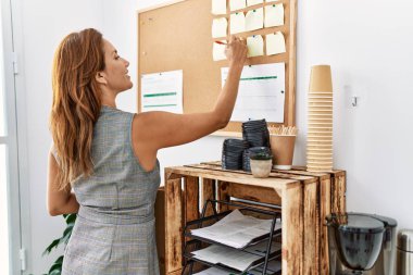 Genç Latin iş kadını ofiste mantar panoya yazı yazıyor.