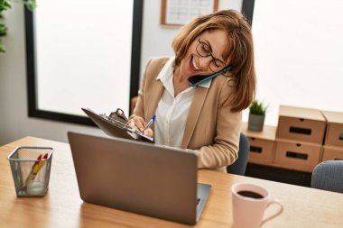 Genç beyaz iş kadını ofiste çalışan akıllı telefondan konuşuyor..