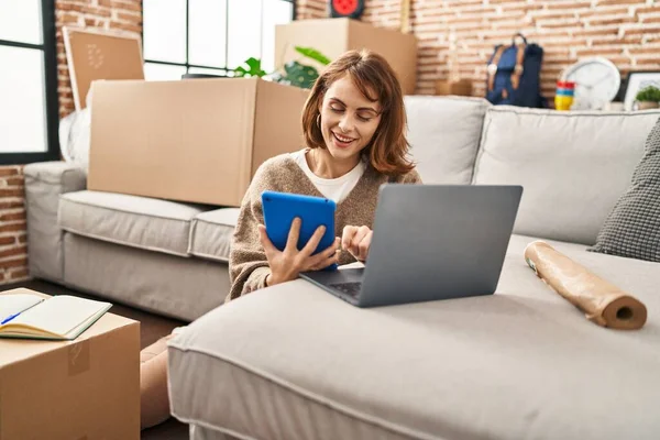 Yeni evinde dokunmatik ped ve dizüstü bilgisayar kullanan beyaz bir kadın gülümsüyor.