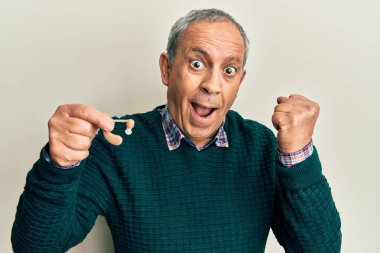 Gri saçlı, elinde tıbbi işitme cihazı olan yakışıklı bir adam gururla bağırıyor, zaferi ve başarıyı kutluyor. 