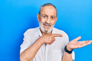 Sakallı, sıradan beyaz tişörtlü yakışıklı bir adam kameraya hayret ediyor ve gülümsüyor.. 