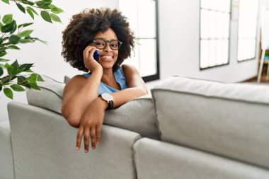 Genç Afrikalı Amerikalı kadın gülümsüyor. Kendine güveni tam. Evde akıllı telefondan konuşuyor.